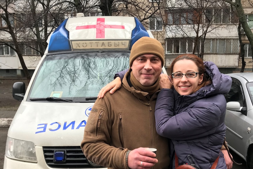A man and a woman hugging in front of an ambulance