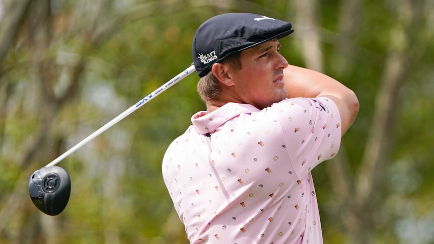 Bryson DeChambeau holds a pose with his driver behind him after hitting a shot