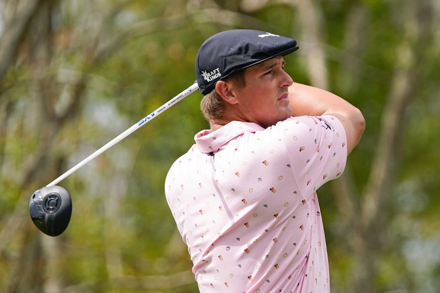 Bryson DeChambeau tient une pose avec son chauffeur derrière lui après avoir frappé un coup