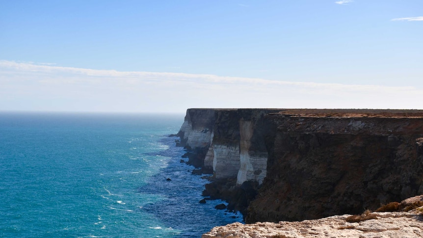 Large sea cliffs with different colours.  The water is calm and the sky is blue.
