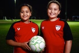 Two girls smile and hold a football at training.