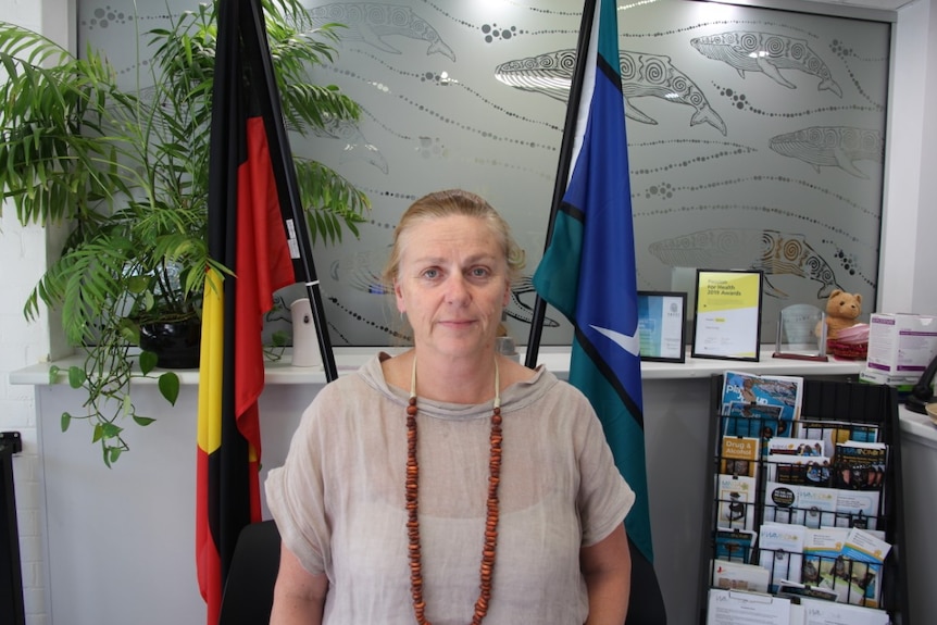 A woman with beads around her neck standing between two flags in an office.