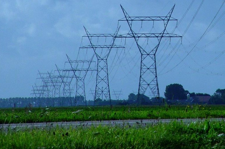 A seemingly never-ending series of huge power pylons stretching through green fields and off into the distance.