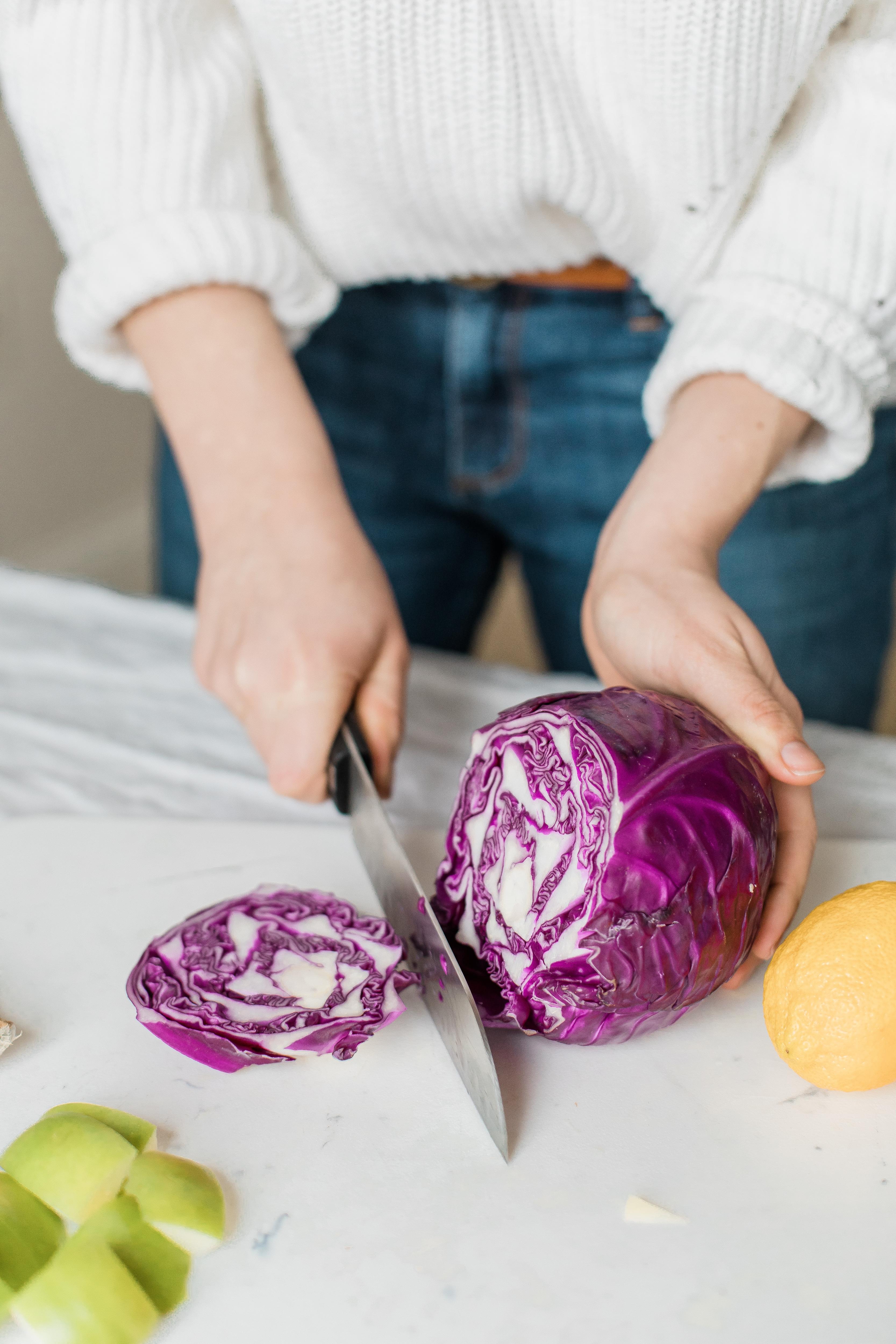 A close up photo of a woman chopping a purple cabbage