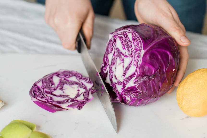 A close up photo of a woman chopping a purple cabbage