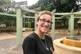 Sarah Lucock, with glasses and a black t-shirt, smiles while standing in a park.