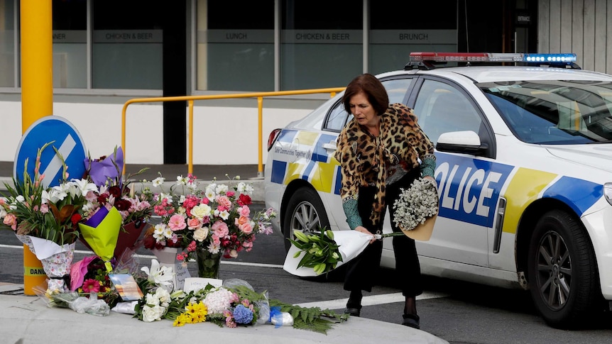 A woman wearing a leopard print top lays flowers on a traffic island, in front of a police car.