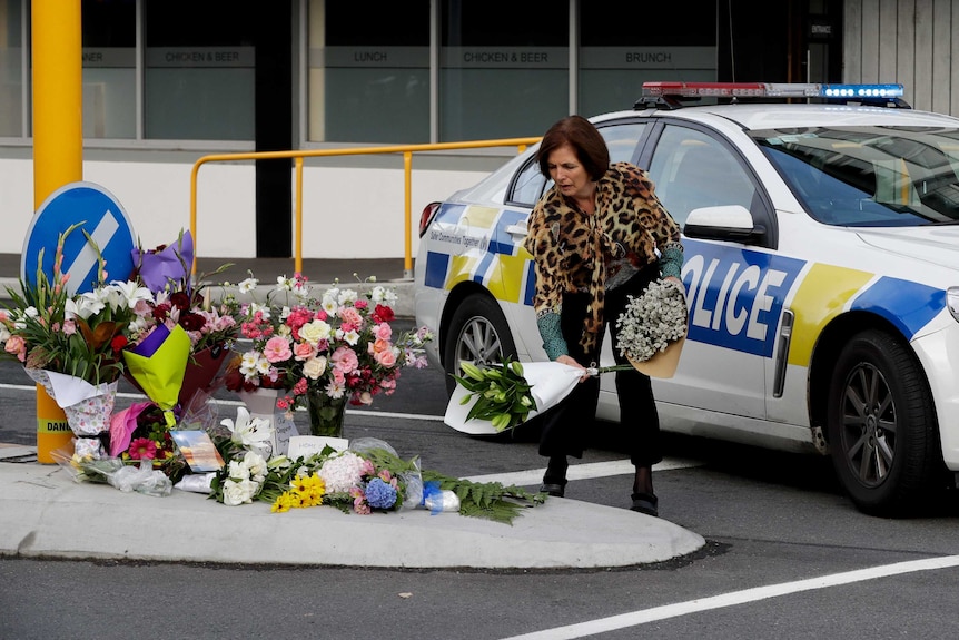 A woman wearing a leopard print top lays flowers on a traffic island, in front of a police car.
