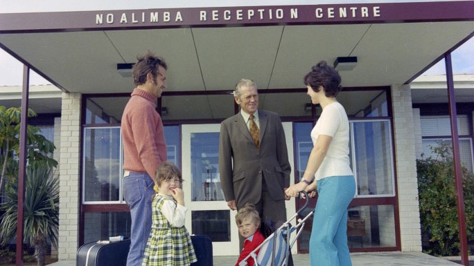 Couple with young children greeted by older man at entrance
