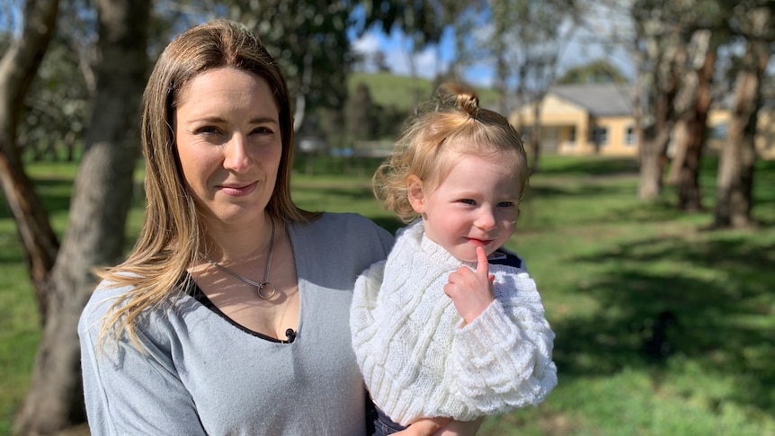 A young woman holding her young child outside by some trees