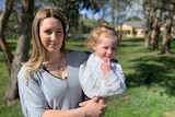 A young woman holding her young child outside by some trees