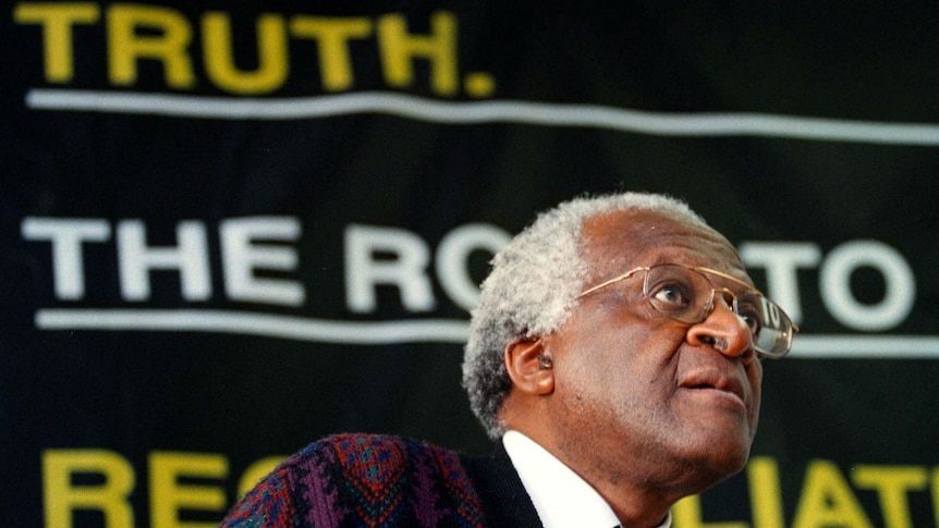 El arzobispo Desmond Tutu se ve pensativo con un traje marrón con la palabra 