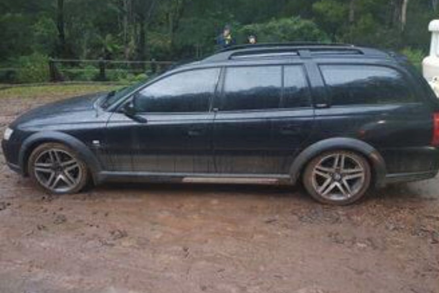 A dark coloured station wagon parked at a camping ground.