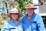 Two people wearing blue work shirts and wide brimmed hats look at the camera.