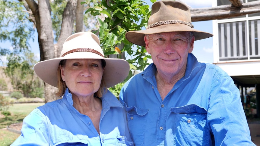 Two people wearing blue work shirts and wide brimmed hats look at the camera.