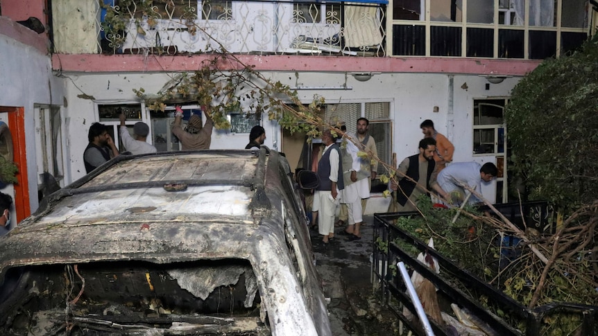 Afghans inspect car wreckage and damage of house after drone strike. 