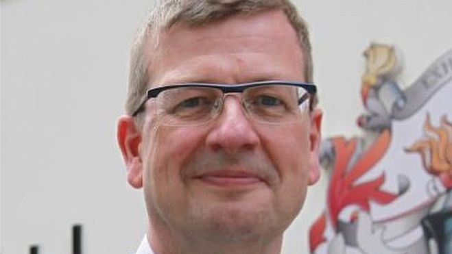 An image of a man in a suit wearing glasses.