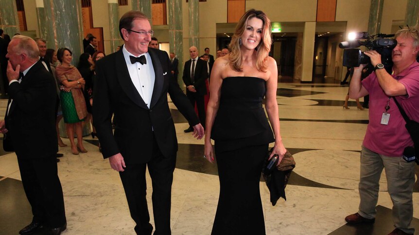 A couple in black tie attire smile for cameras in the marble foyer of Parliament House.