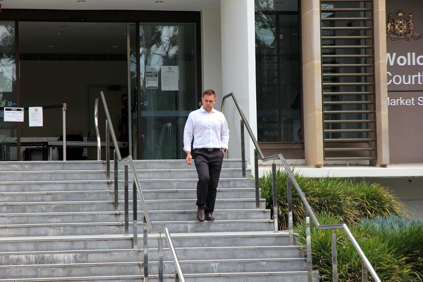 A man in suit pants and a white shirt descends a set of stairs outside a court building.