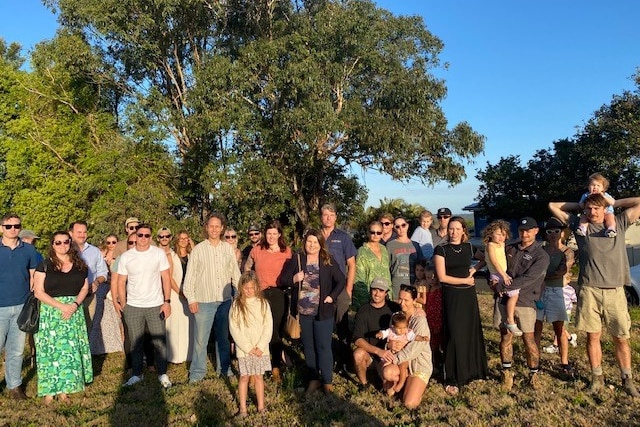 A large group of people stand under a tree