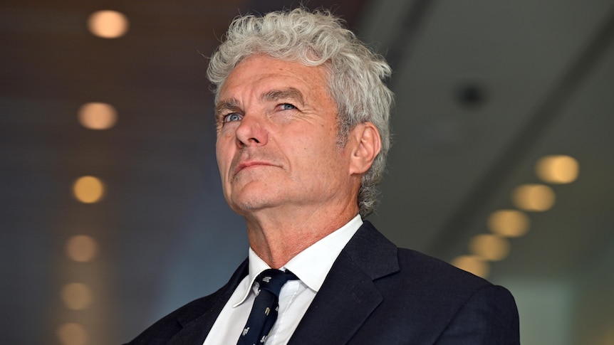 A close up shot of a man with white hair wearing a suit. 