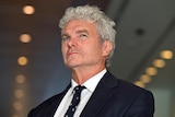 A close up shot of a man with white hair wearing a suit. 