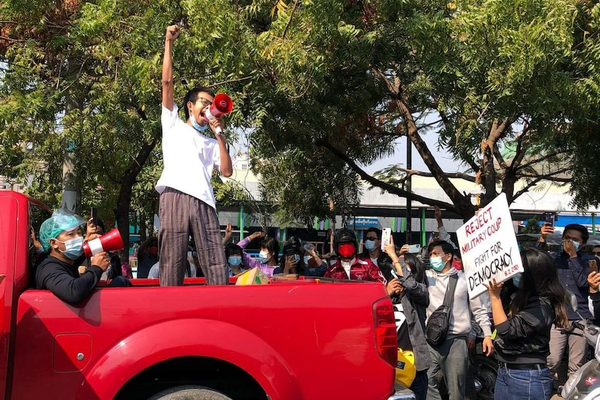 Tayzar San stands with a fist in the air on the back of a red truck and speaks into a megaphone