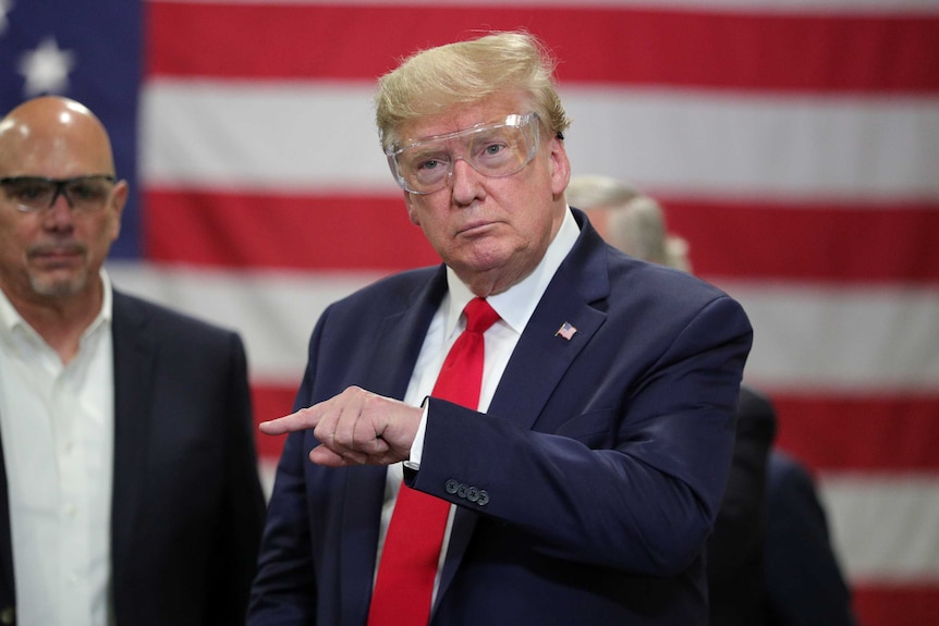 Donald Trump wears protective goggles with a US flag in the background