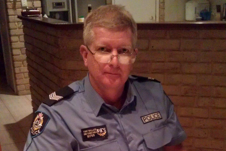 A man in a police uniform sits at a wooden desk in a police station