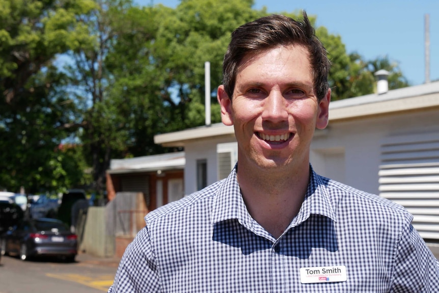 A clean shaven man with short brown hair, wearing a blue and white checked shirt with a Labor party name tag.