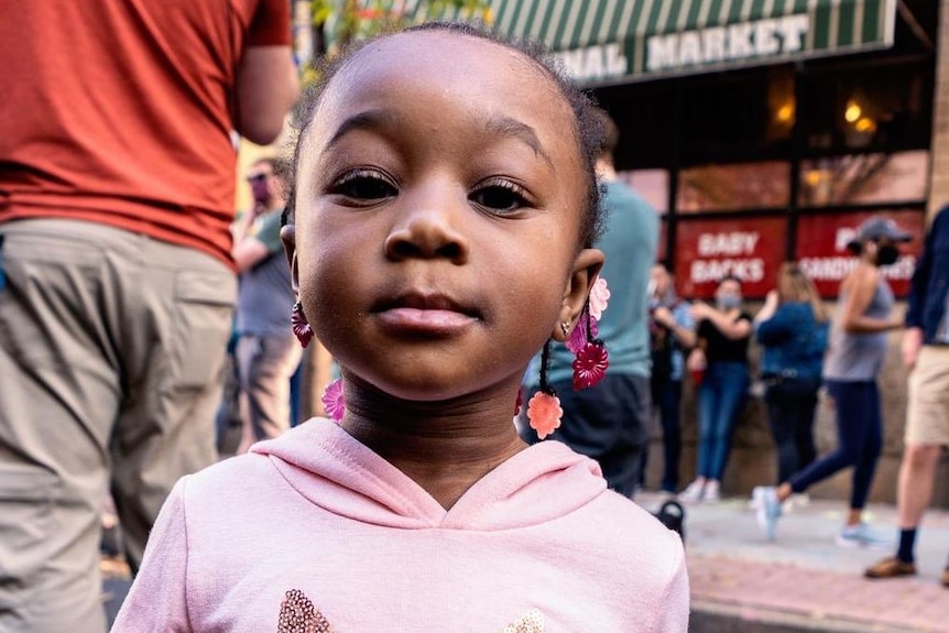 A little African American girl in a pink hoodie standing on a street