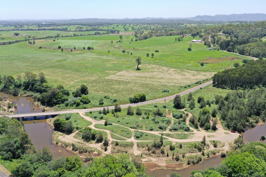 An aerial view of a river bend with multiple twisting, bare dirt tracks cut into the land beside it. 