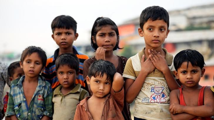 Seven Rohingya refugee children dressed in tattered clothing at a refugee camp in Cox's Bazar, Bangladesh, stare into distance