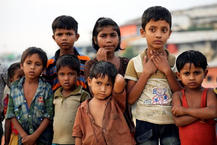Seven Rohingya refugee children dressed in tattered clothing at a refugee camp in Cox's Bazar, Bangladesh, stare into distance