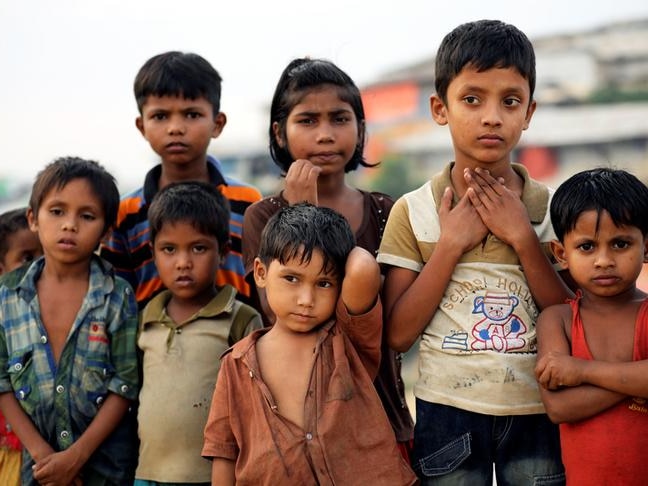 Seven Rohingya refugee children dressed in tattered clothing at a refugee camp in Cox's Bazar, Bangladesh, stare into distance