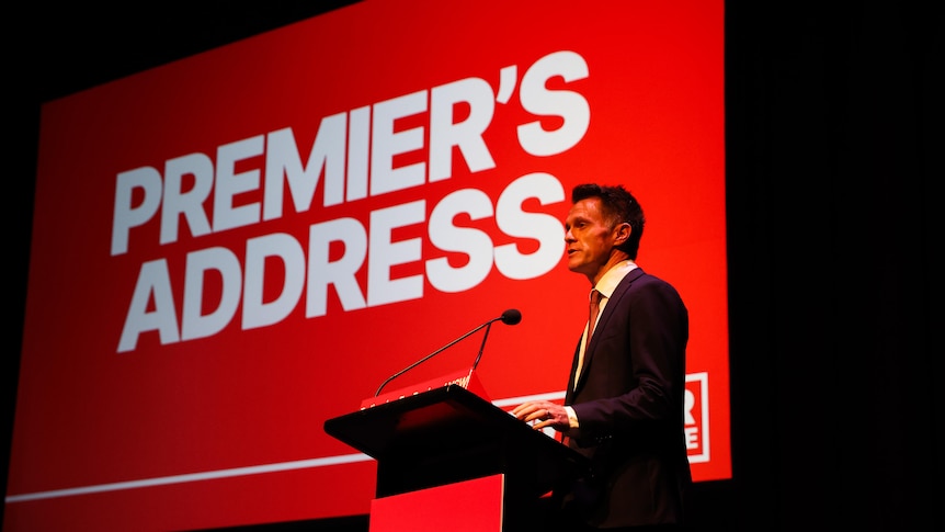 A man in a dark suit – Chris Minns – speaks in front of a backdrop that says "Premier's Address".