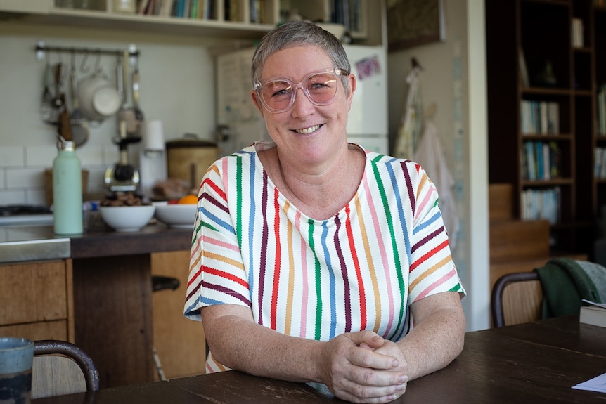 Woman in striped top and glasses sitting at table smiling at camera.