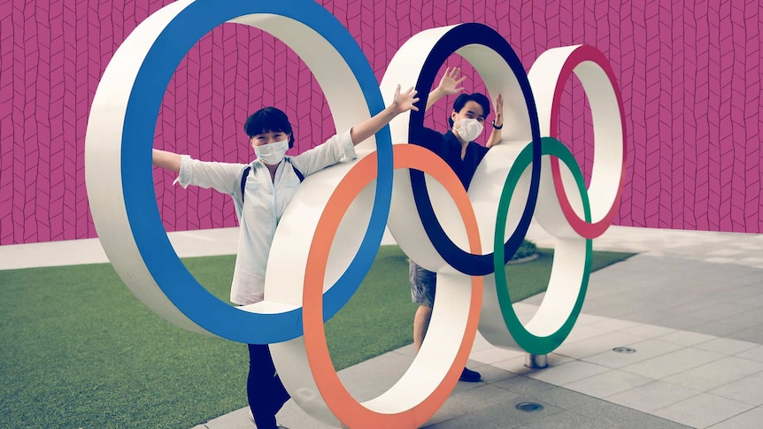 Visitors wearing protective face masks pose for a photo through the Olympic rings.