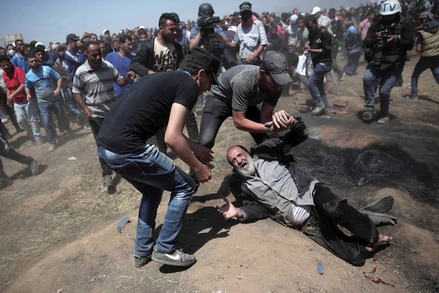 Two men assist an elderly Palestinian man who fell on the ground after being shot.