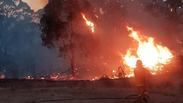 A firefighter points a hose at a bushfire near Hepburn.