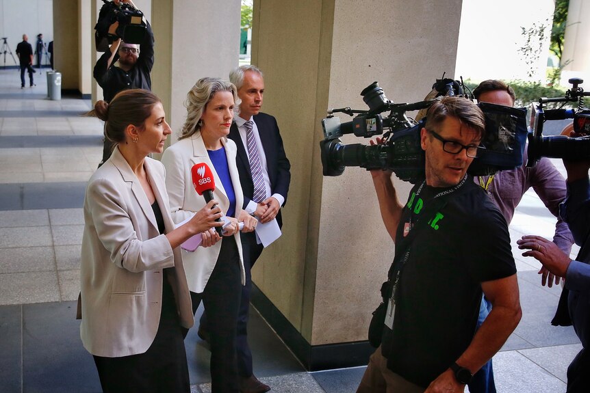 Clare O'Neil and Andrew Giles are followed by media after leaving a press conference at parliament house