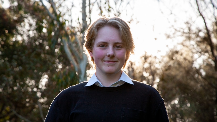 A teenager with short blonde hair smiles at the camera