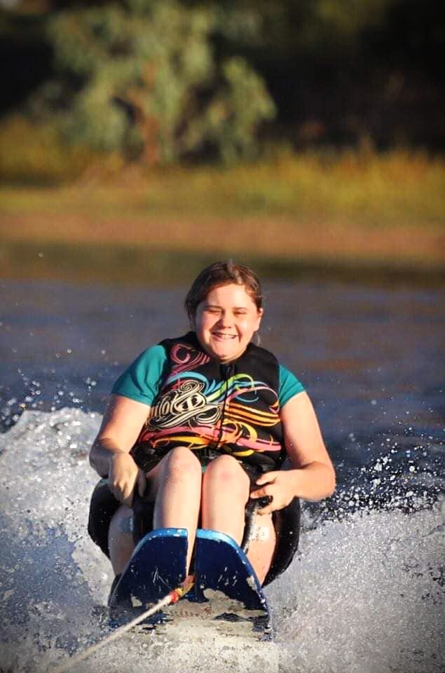 A woman sits on an assisted water ski, laughing out on the water 