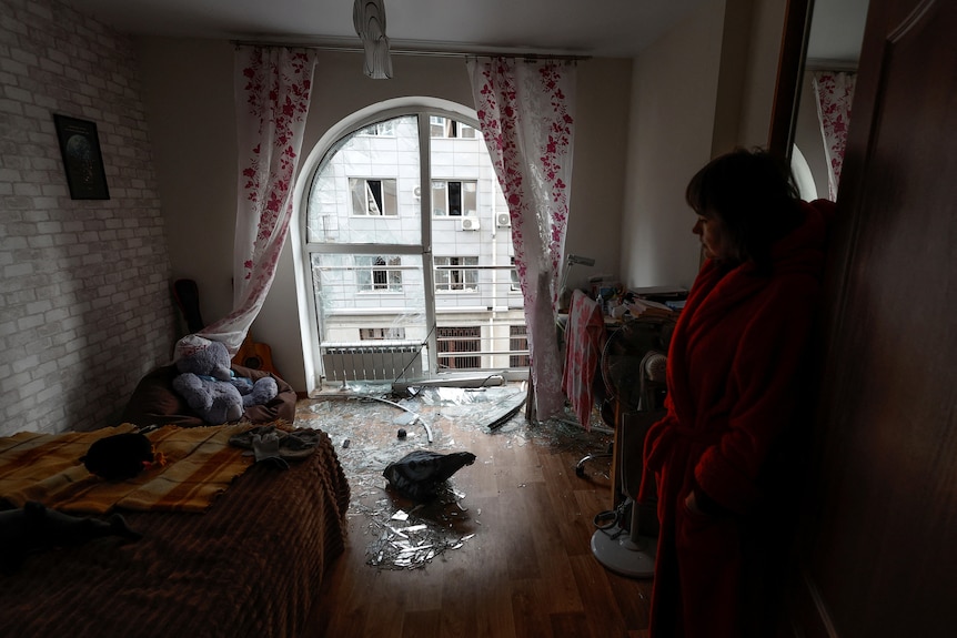 Woman shows living room damaged by shrapnel from a Russian air strike. 