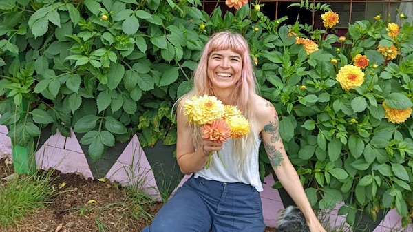 Hannah sitting in a garden holding a bunch of yellow and orange dahlia flowers.