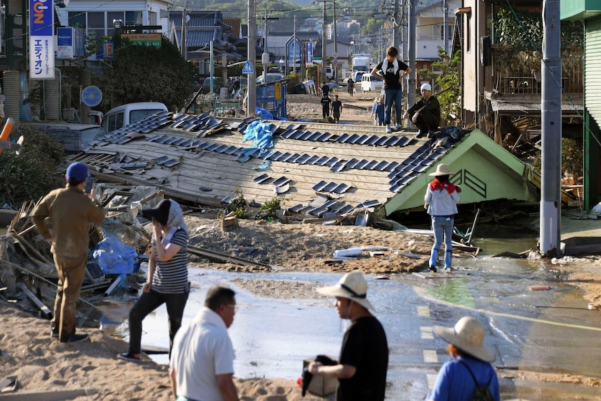 People wear hats, standing in street devastated by flood