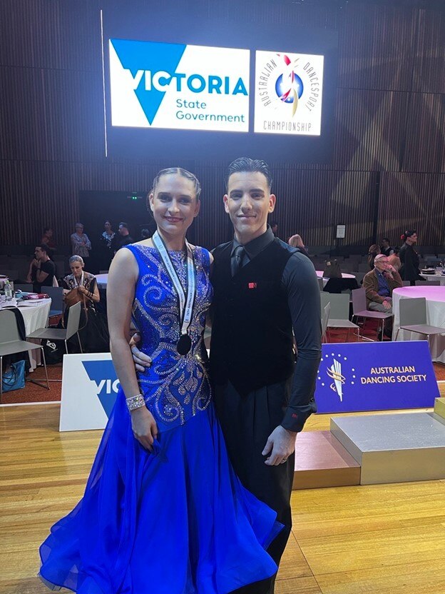 Vanessa wearing blue gown with sparkly, silver swirls and medal around her neck with arm around a man in tie and vest.