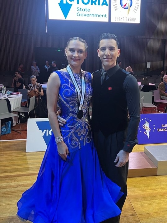 Vanessa wearing blue gown with sparkly, silver swirls and medal around her neck with arm around a man in tie and vest.