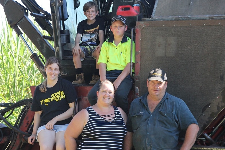 Farron Bowman and his wife stand in front of a harvester with their children sitting behind them.