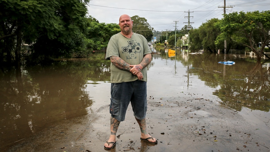 A man standing in front of flood waters in Lismore.